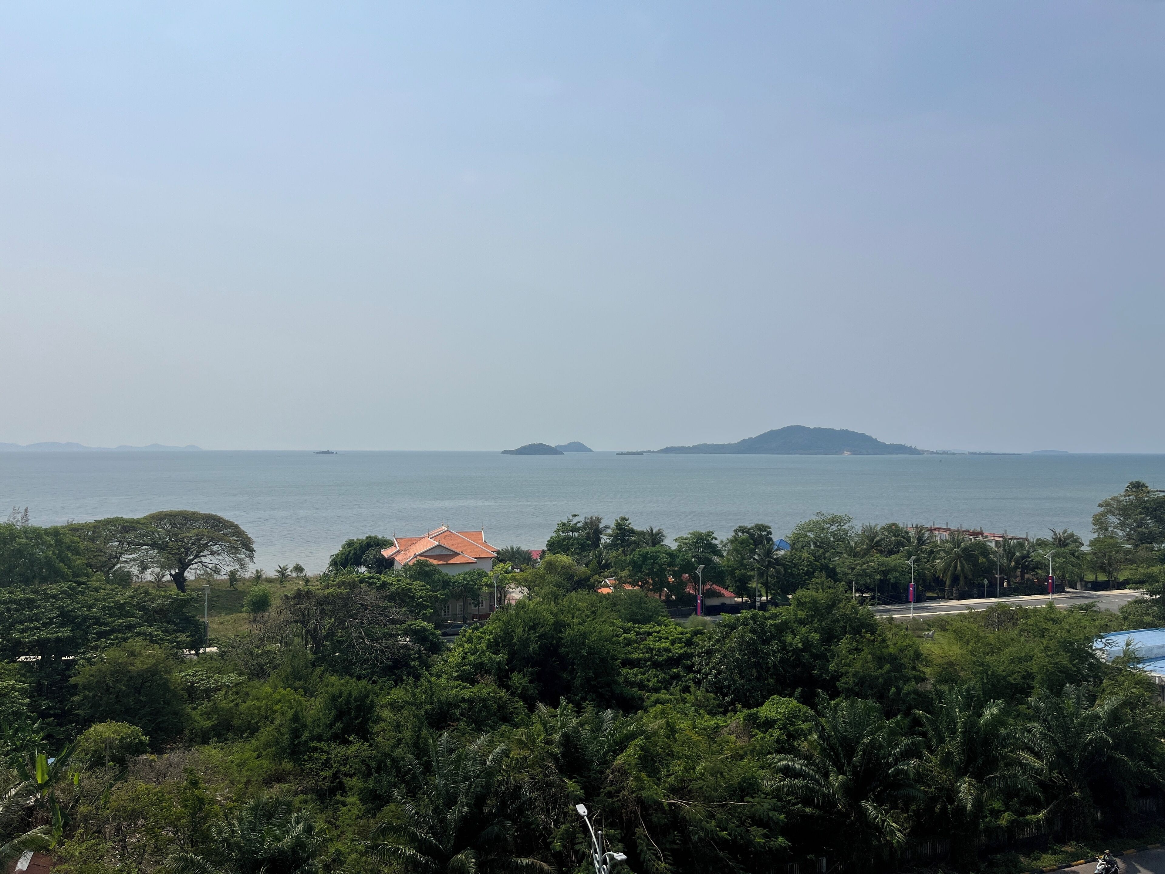 A coastal landscape with dense greenery, a body of water, and distant islands.