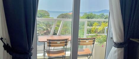 A balcony with two wooden chairs and a table, overlooking a scenic view of greenery and a distant shoreline.