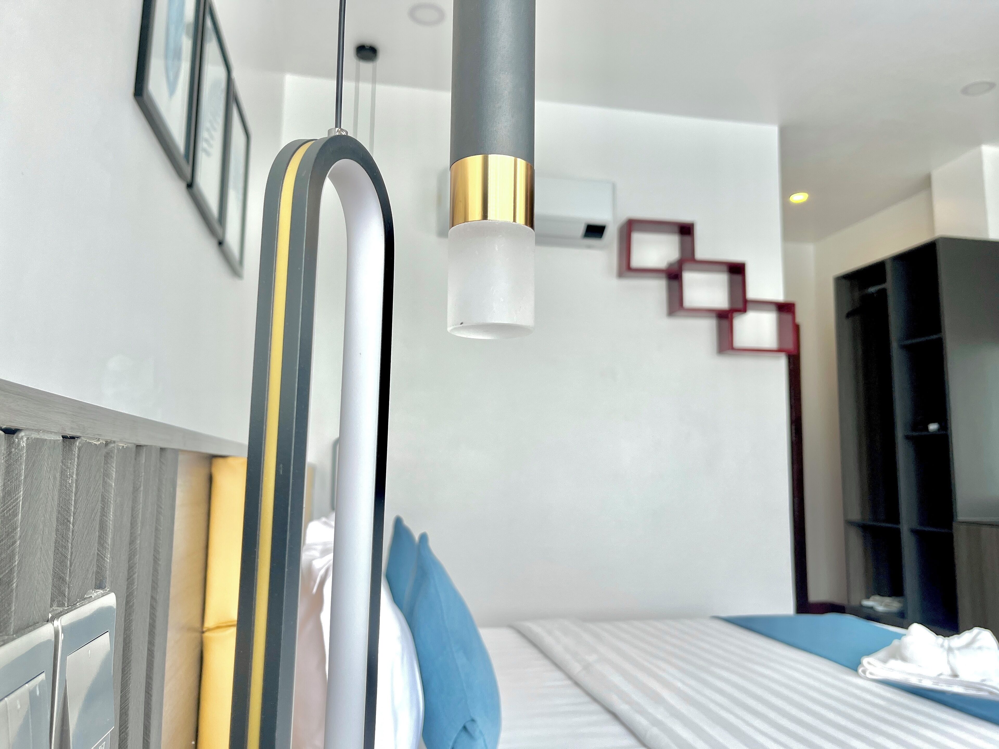 Una habitación de hotel moderna con una cama, una mesita de noche, una lámpara de pared y un adorno geométrico rojo.