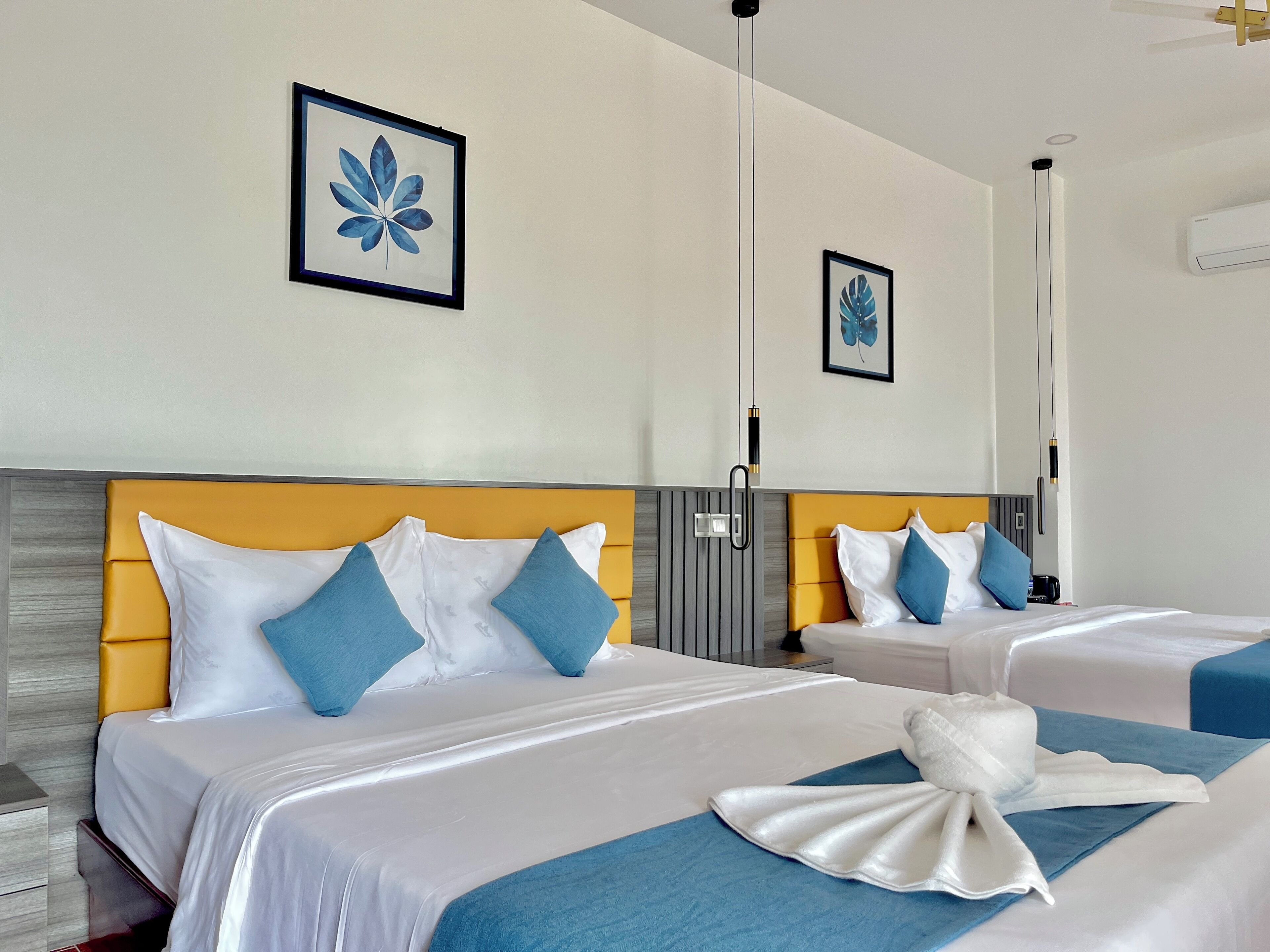 A hotel room with two beds, each with white bedding and blue pillows, a wooden headboard, and a blue accent wall.
