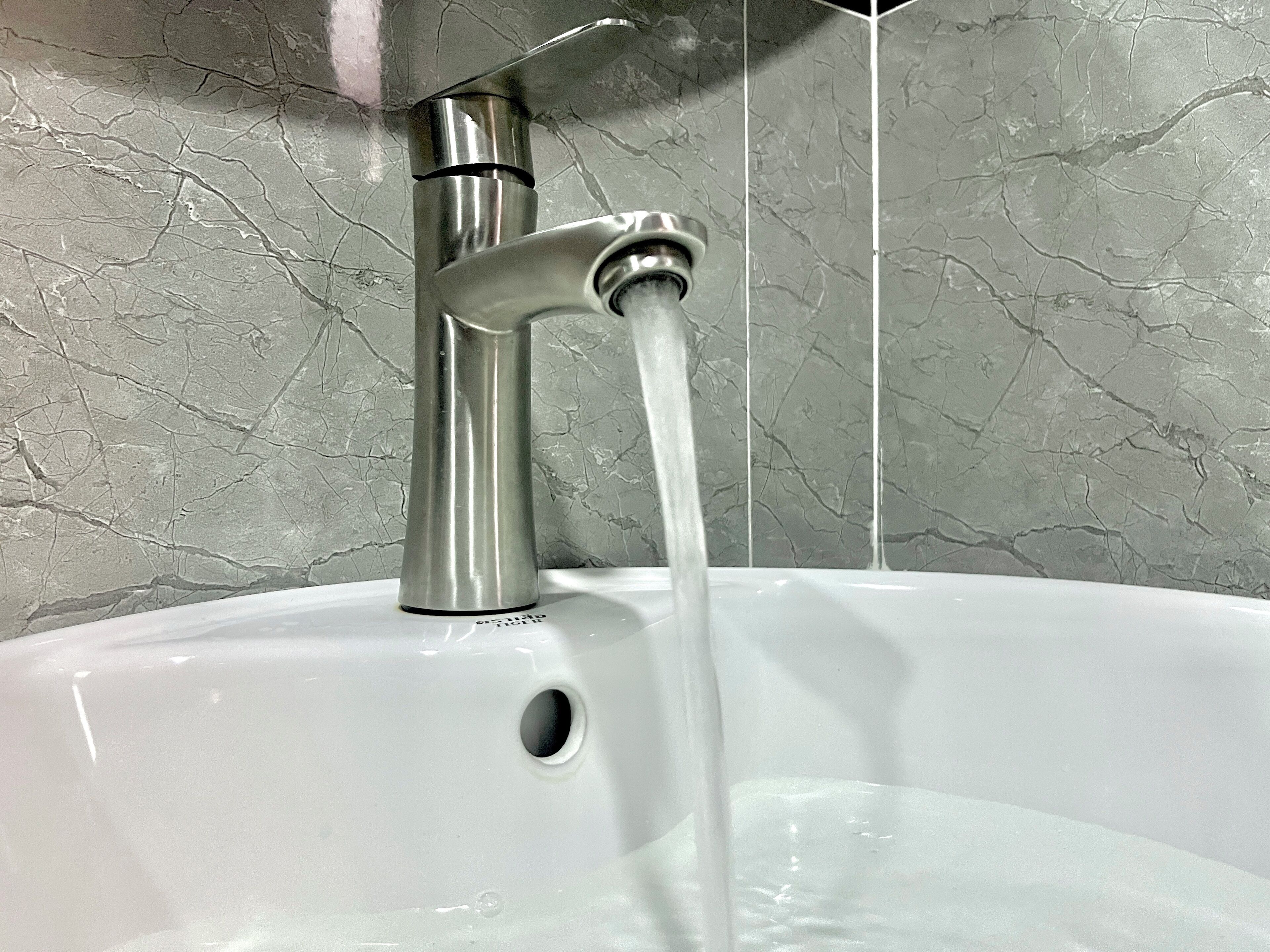 Un lavabo con l'acqua corrente, un rubinetto e una parete in marmo.
