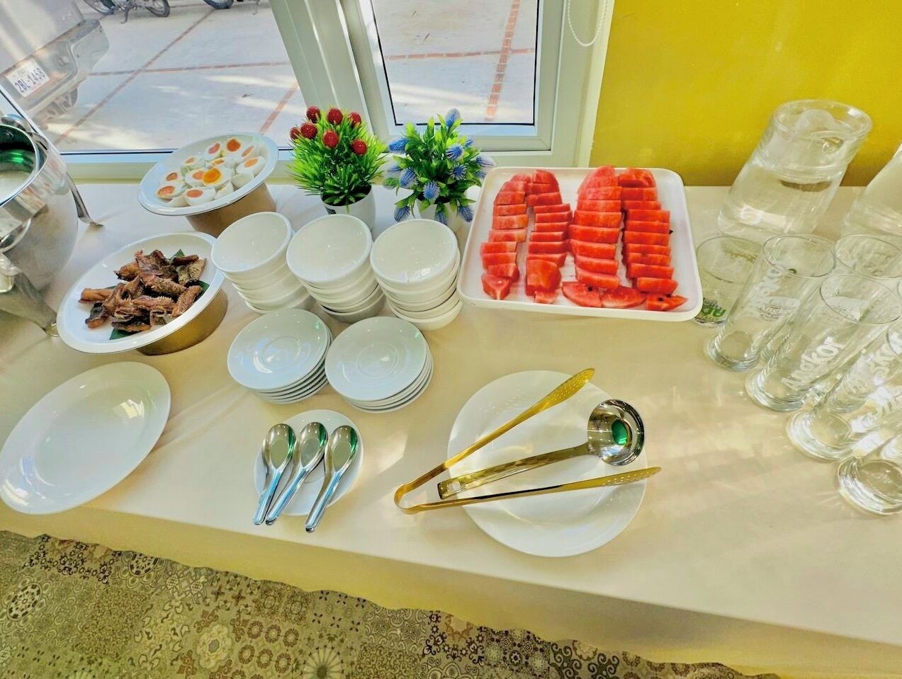 Uma mesa de buffet com pratos de comida, talheres e copos.