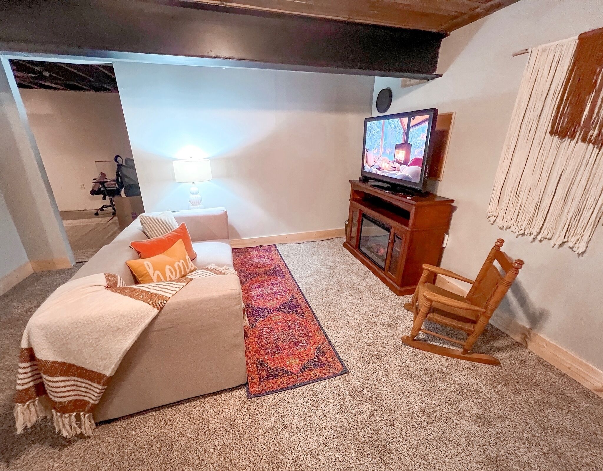 A cozy living room with a sofa, a television, a wooden chair, a rug, and a lamp.