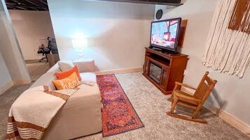 A cozy living room with a sofa, a television, a wooden chair, a rug, and a lamp.