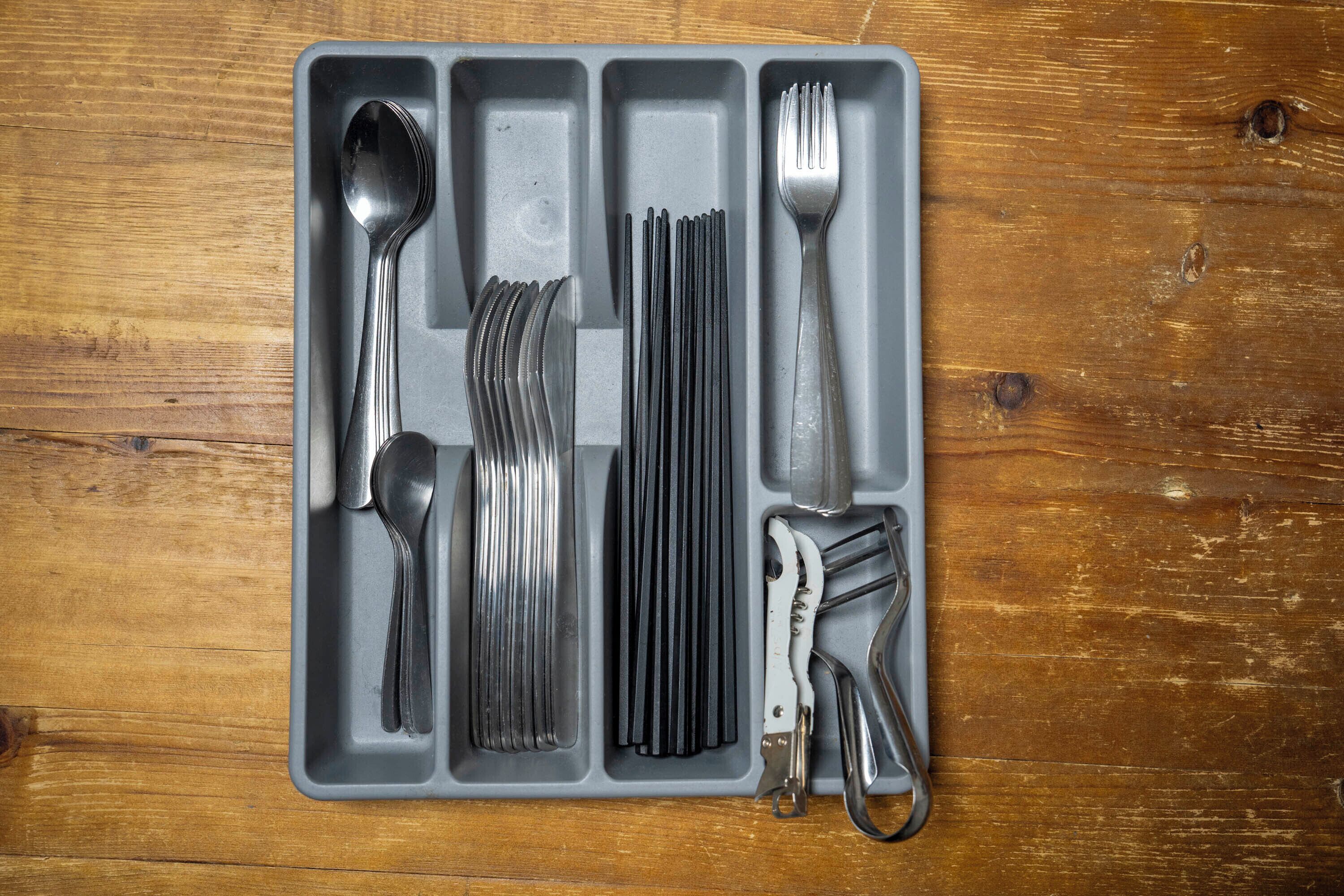 A gray tray with various utensils including a spoon, fork, knife, and a pair of scissors.