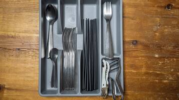 A gray tray with various utensils including a spoon, fork, knife, and a pair of scissors.