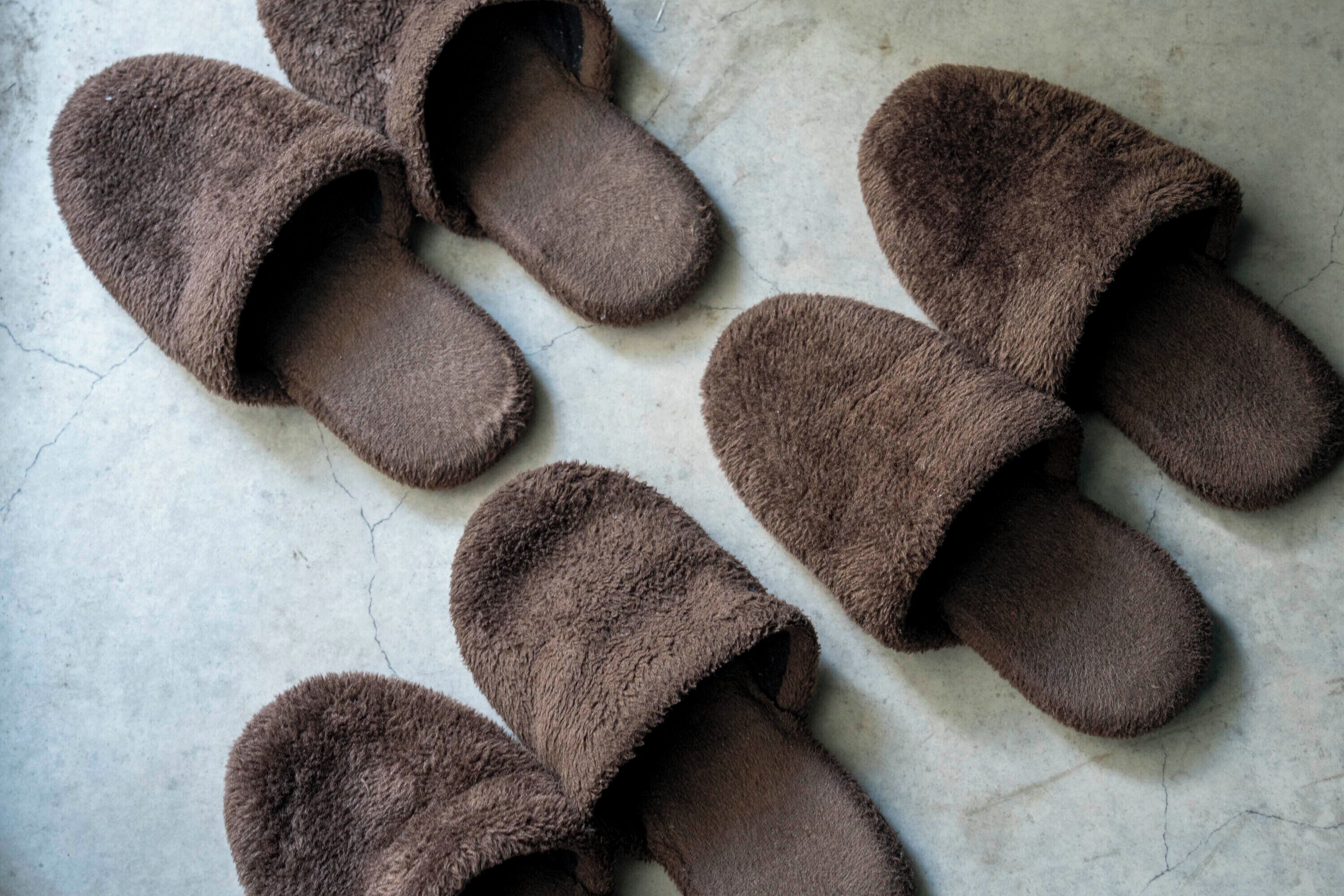 A pair of brown slippers with fuzzy texture, placed on a cracked concrete floor.
