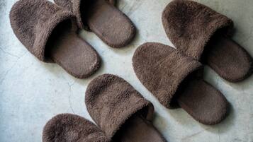 A pair of brown slippers with fuzzy texture, placed on a cracked concrete floor.