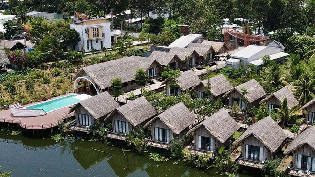 Een resort op water met rieten huisjes, een zwembad en weelderige begroeiing.
