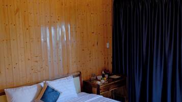 Une pièce aux murs lambrissés, comprenant un lit, un bureau et un luminaire suspendu.