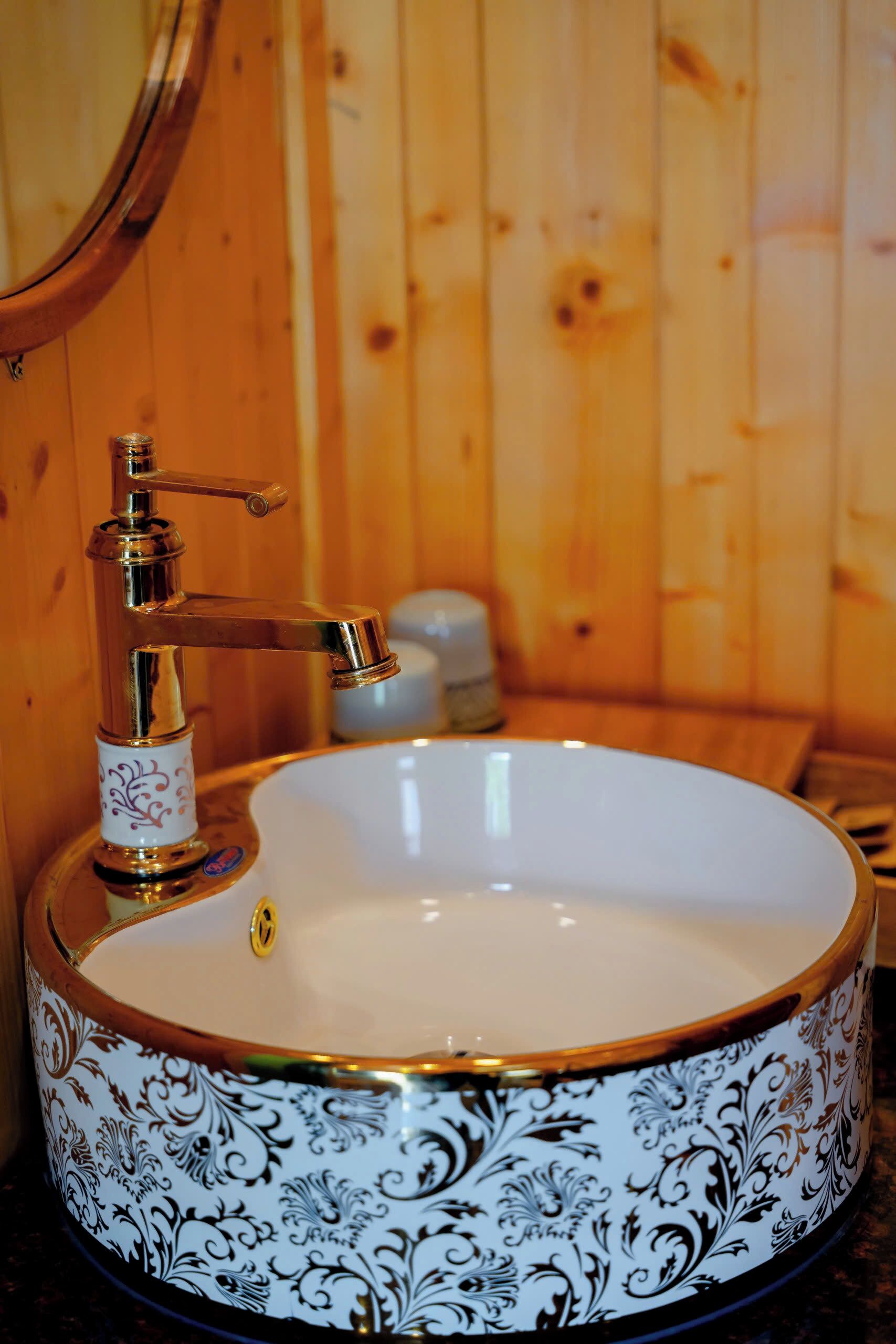 A bathroom with a round sink, a gold faucet, and a wooden background.