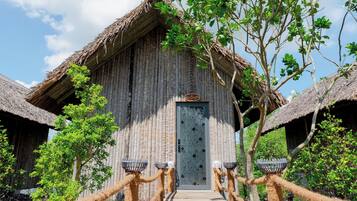 A rustic wooden building with a thatched roof, a decorative door, and rope barriers leading to the entrance.