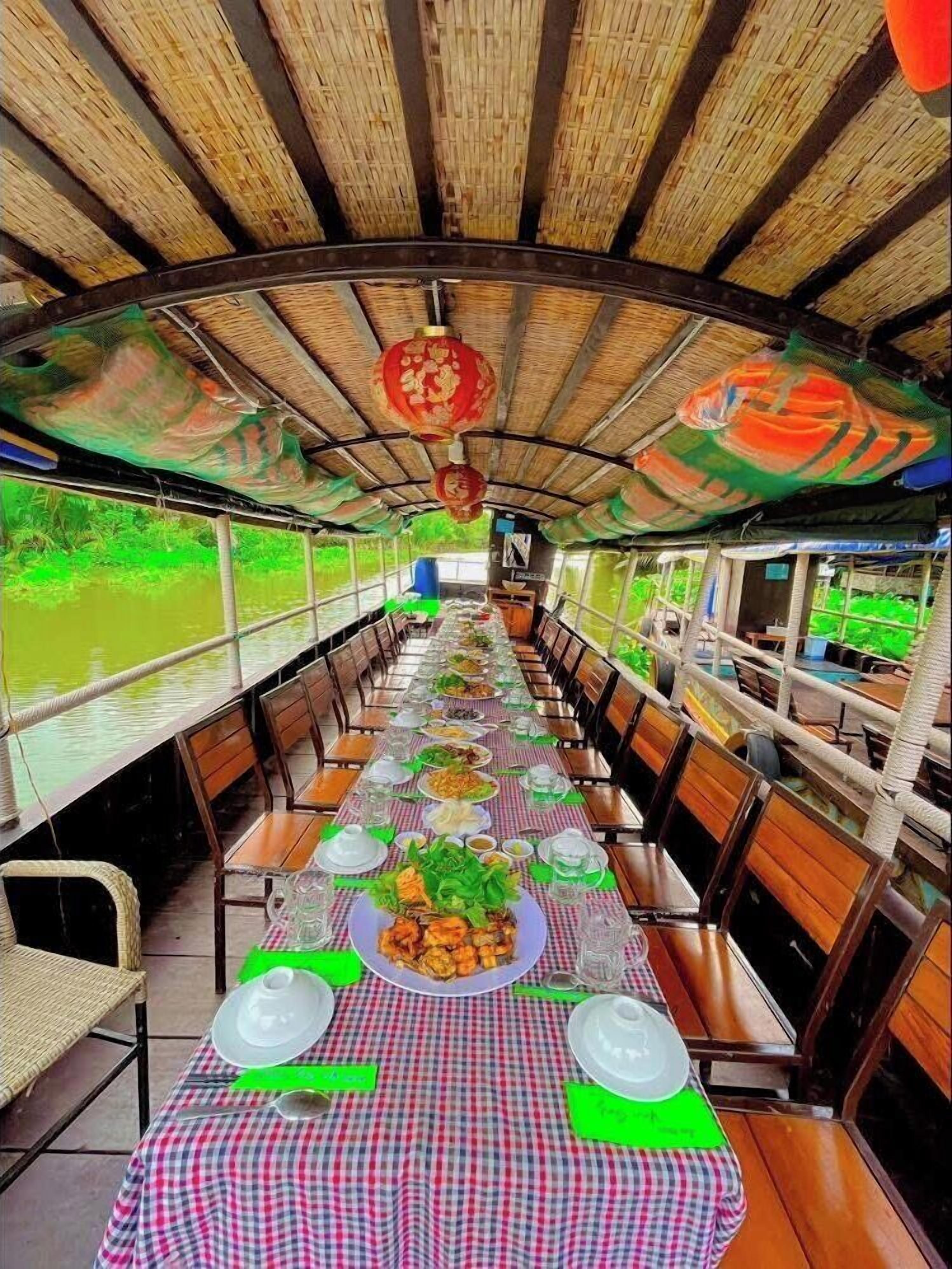 Un espace de restauration aménagé sur un bateau, avec une nappe à carreaux, des chaises en bois et un toit de chaume.