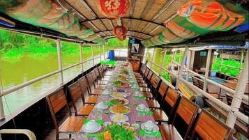 Un espace de restauration aménagé sur un bateau, avec une nappe à carreaux, des chaises en bois et un toit de chaume.