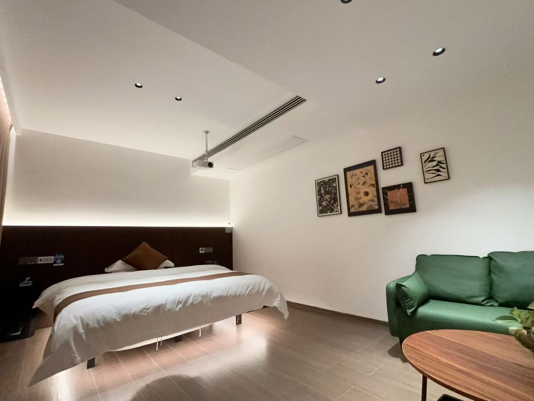 Una habitación de hotel moderna con una cama, un sofá verde, una mesita de madera y cuadros en la pared.
