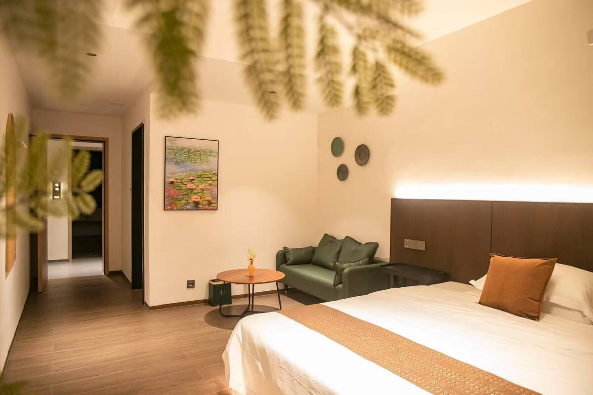 A hotel room with a bed, a green sofa, a small round table, and a painting on the wall.