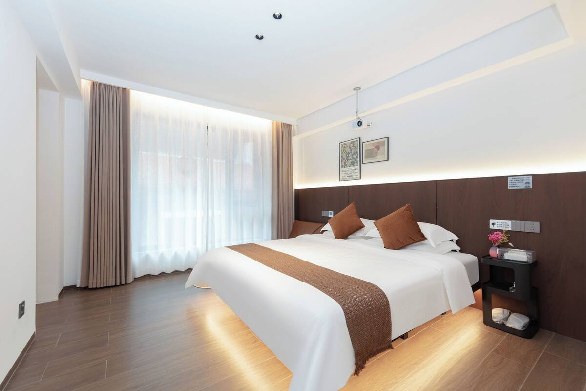A modern hotel room with a large bed, a nightstand, and a wall-mounted control panel.