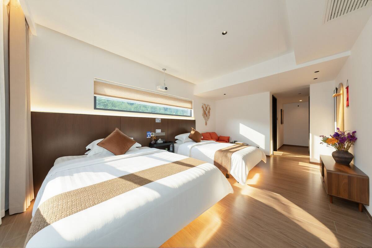 A modern hotel room with two beds, a large window, a flat-screen TV, and a wooden floor.