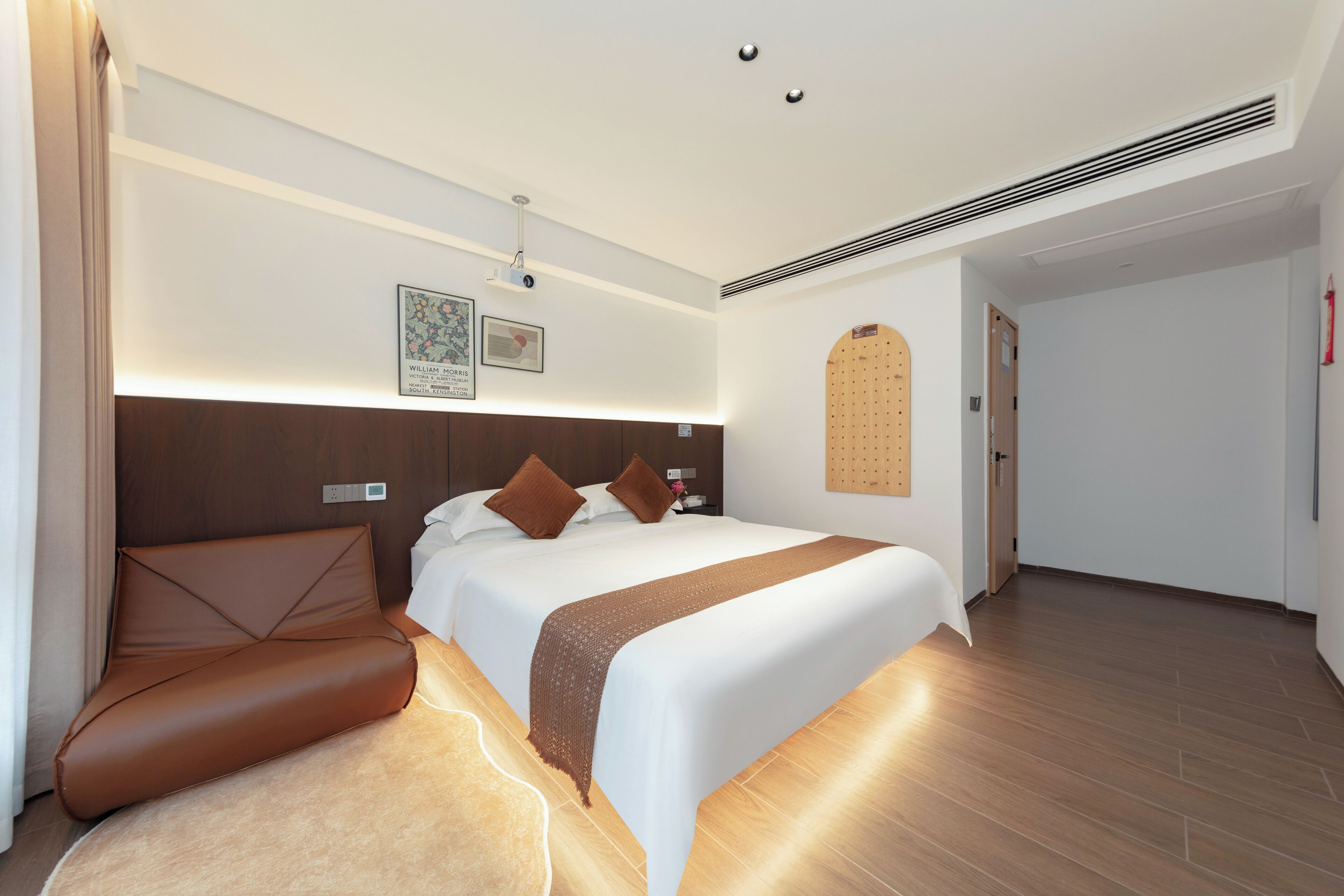 A modern hotel room with a large bed, a brown leather sofa, and a wooden headboard.