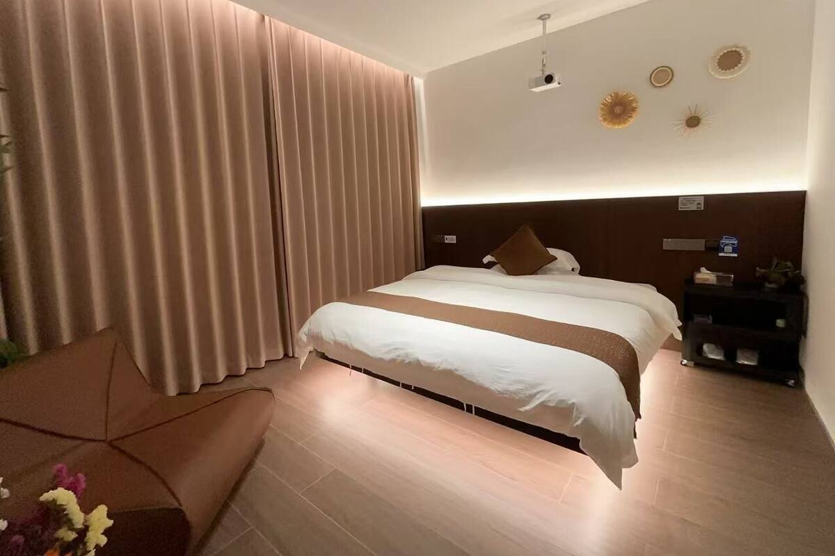 A modern hotel room with a large bed, a bedside table, and a wall-mounted projector.