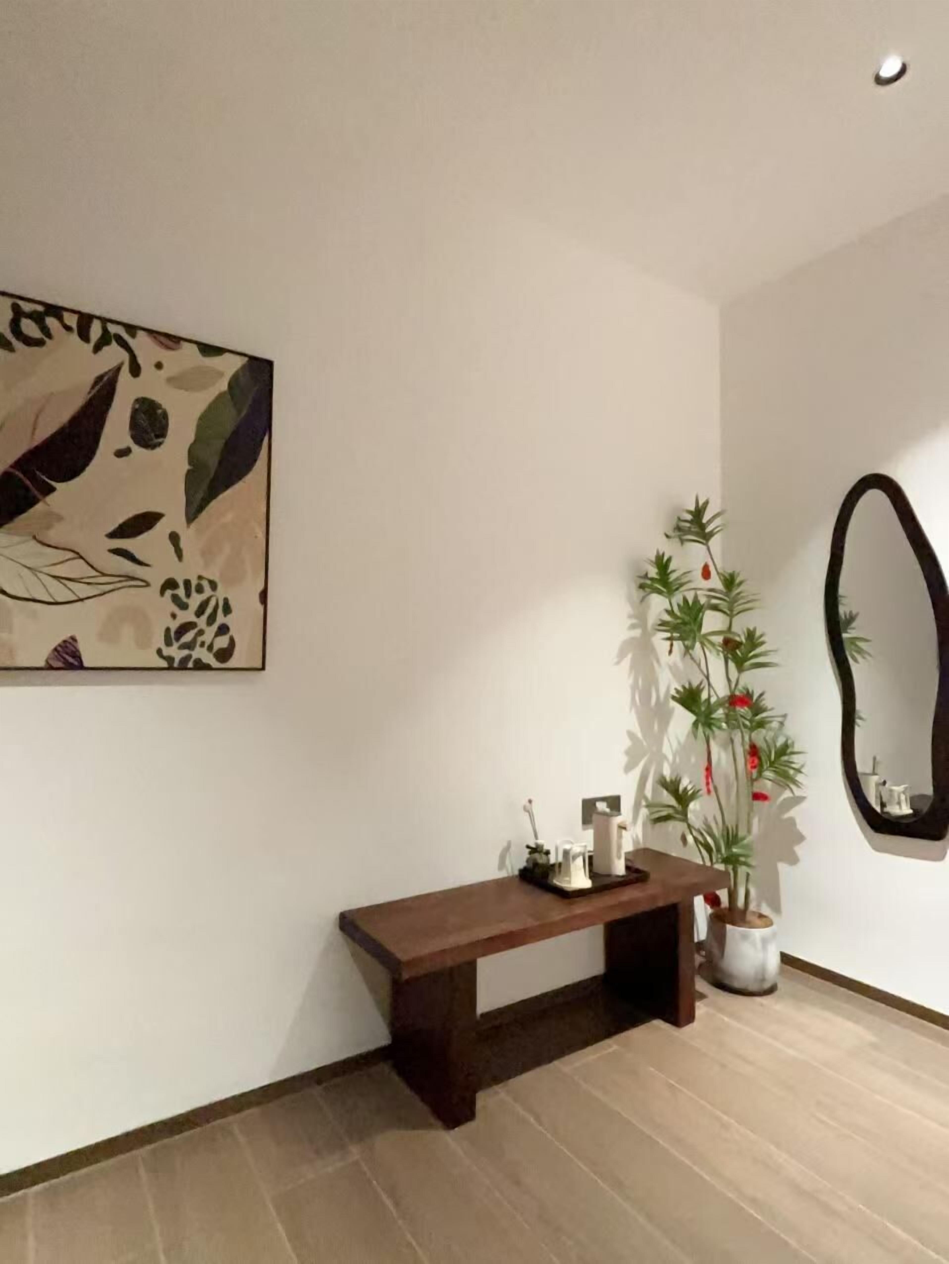 A room with a wooden bench, a potted plant, a wall-mounted mirror, and a painting.