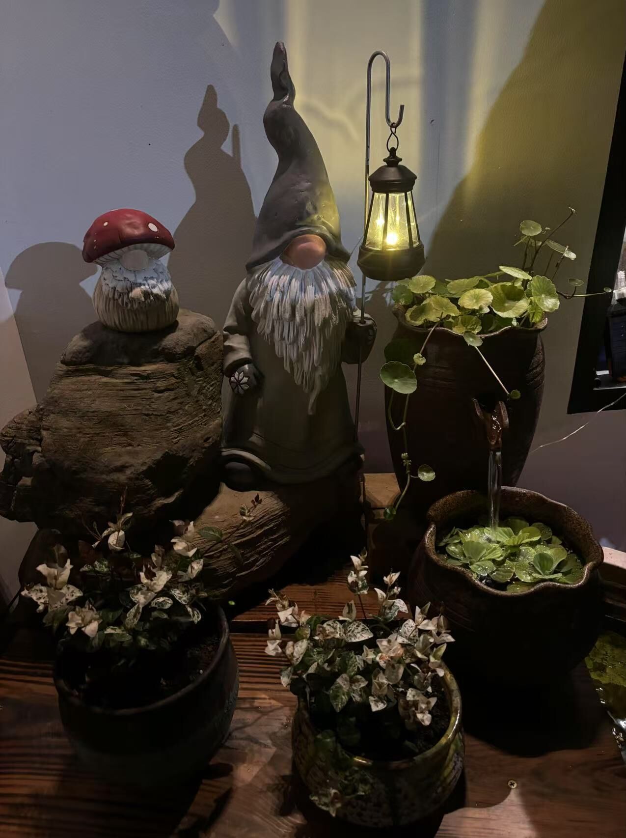 Une collection d’objets décoratifs comprenant un champignon, un gnome, une lanterne et diverses plantes en pot.