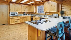 A wooden cabin-style kitchen with a central island, wooden cabinets, and a large window. - Beautiful Log Cabin at Bear Mountain Resort (Big Bear Lake)