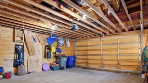 A garage with a concrete floor, wooden beams, a metal garage door, and various tools and equipment. - Beautiful Log Cabin at Bear Mountain Resort (Big Bear Lake)