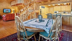 A wooden interior with a dining area featuring a round table, chairs, and a ceiling fan. A staircase leads to an upper level. - Beautiful Log Cabin at Bear Mountain Resort (Big Bear Lake)