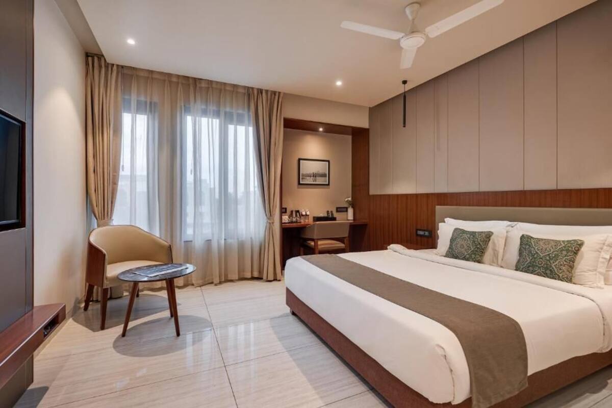 A modern hotel room with a large bed, a desk, a chair, and a television.