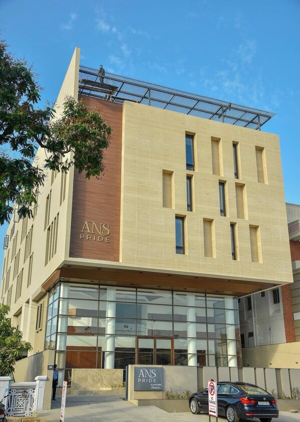A modern building with a prominent 'ANS PRIDE' sign, large windows, and a security guard at the entrance. - HOTEL ANS PRIDE (Pudukkottai)