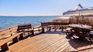 A wooden deck with benches and tables overlooking a body of water, with a large umbrella structure in the background.