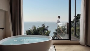 Une salle de bain moderne dotée d’une grande baignoire et d’une porte vitrée donnant sur un balcon avec vue sur la mer.