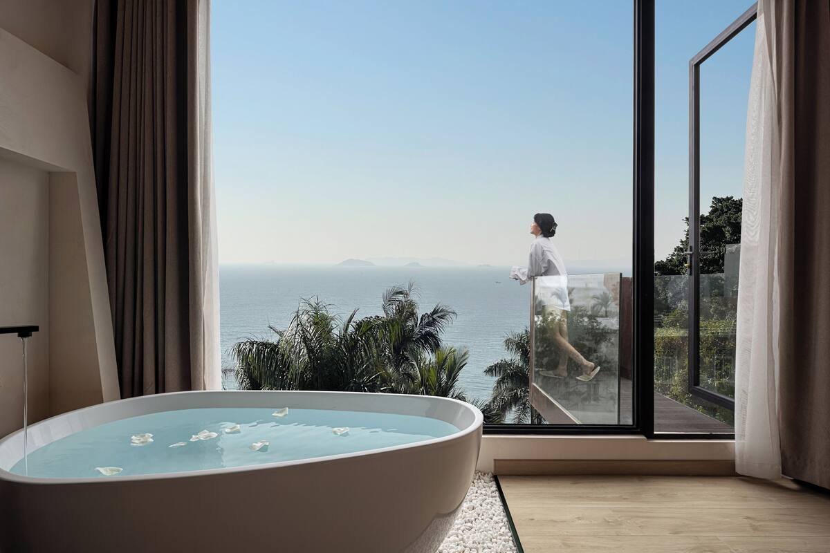 Een moderne badkamer met een groot bad, een glazen deur die leidt naar een balkon met uitzicht op zee.