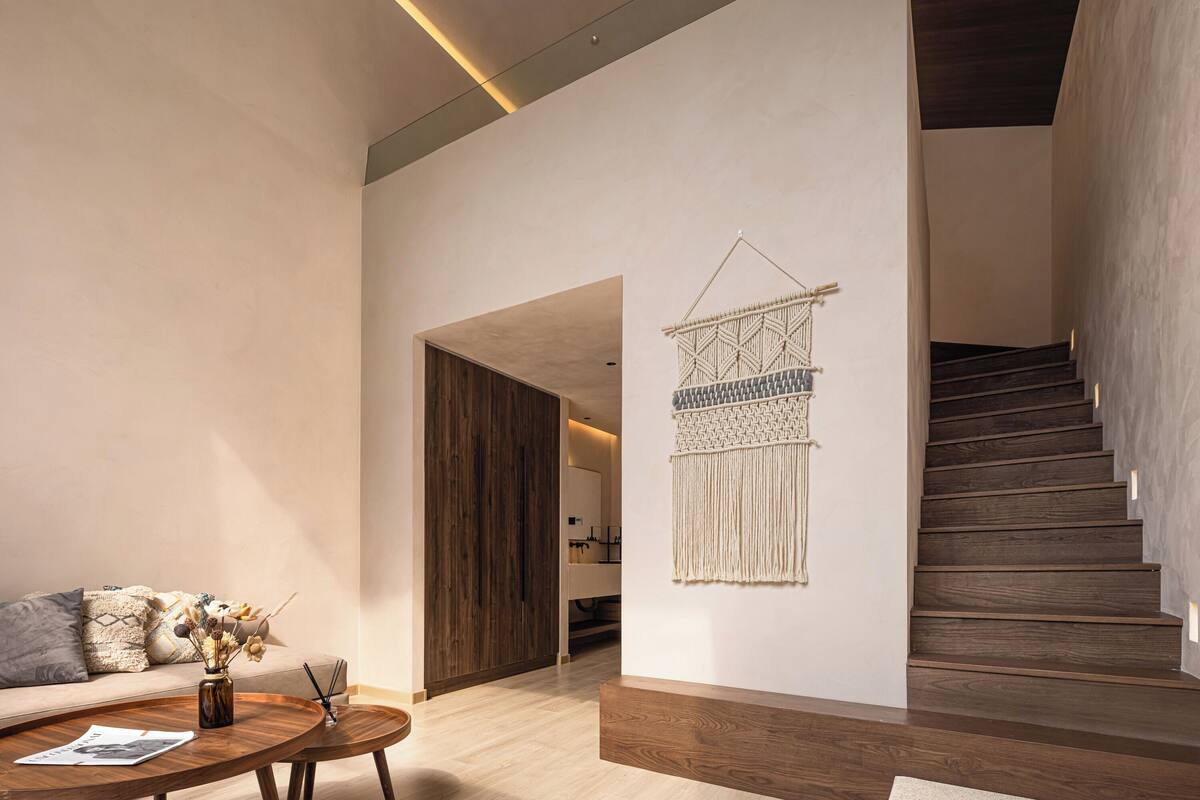 Een modern interieur met een houten trap, wanddecoratie van macramé en een ronde houten salontafel met een tijdschrift.