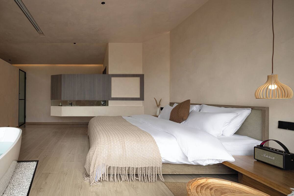Een moderne slaapkamer met een groot bed, een badkuip, een houten nachtkastje en een hanglamp.