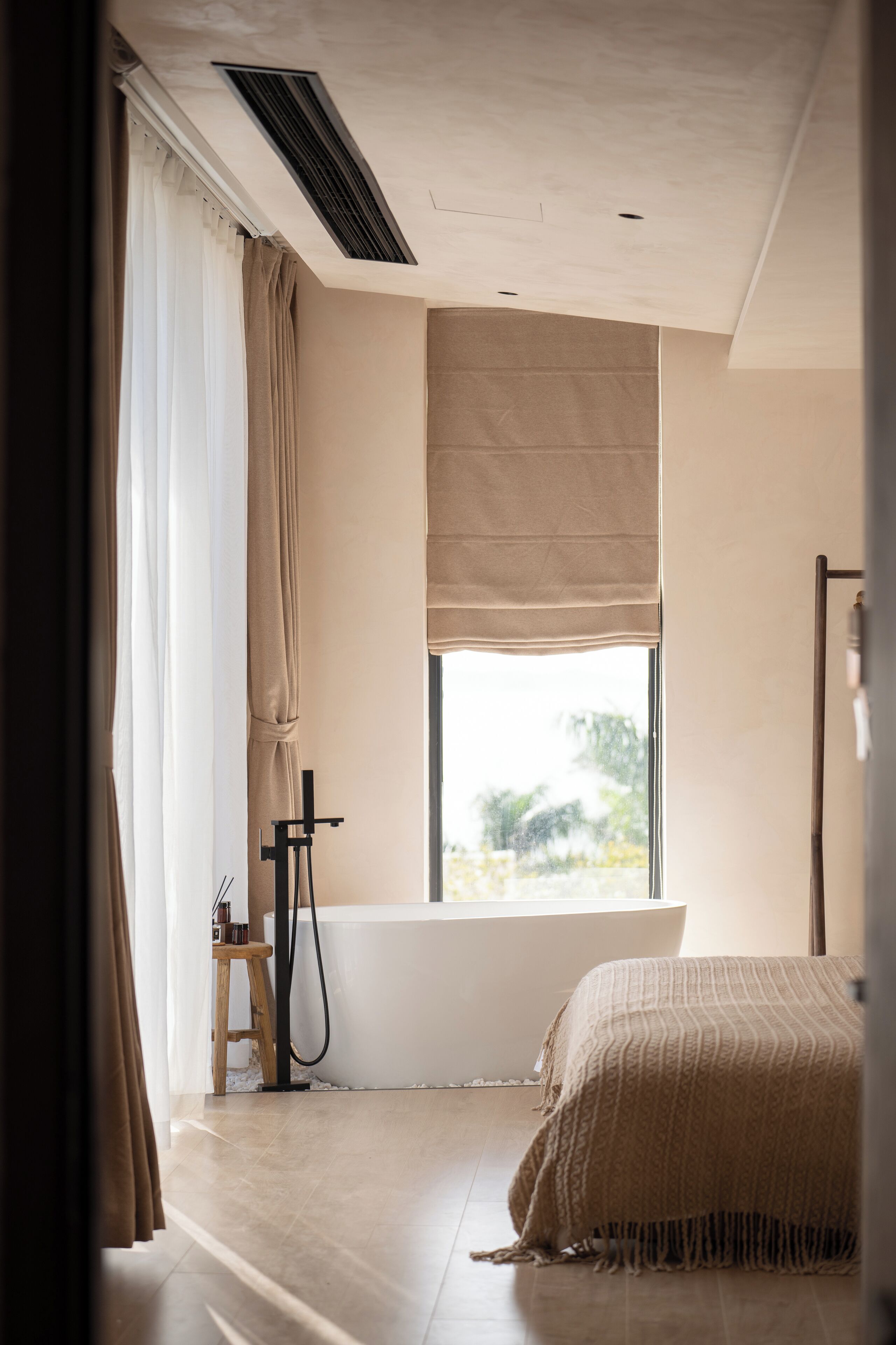 A bedroom with a large window, a bathtub, and a wooden stool.