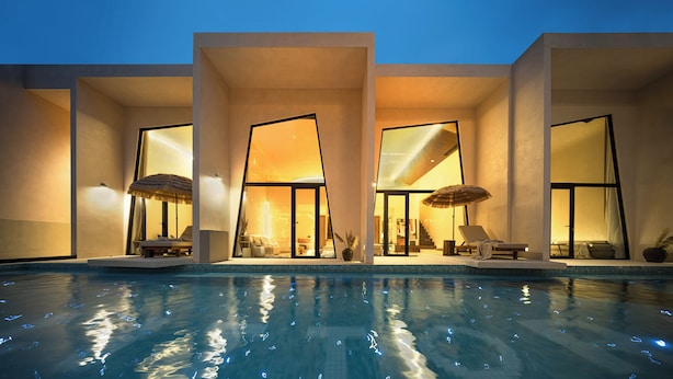 Un hôtel moderne doté d’une piscine, de grandes fenêtres et d’espaces extérieurs aménagés pour se détendre.