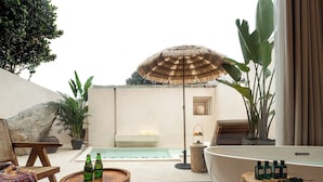Un espace de détente extérieur moderne, doté d’une piscine, de chaises longues, d’une table en bois avec des bouteilles et d’un grand parasol.