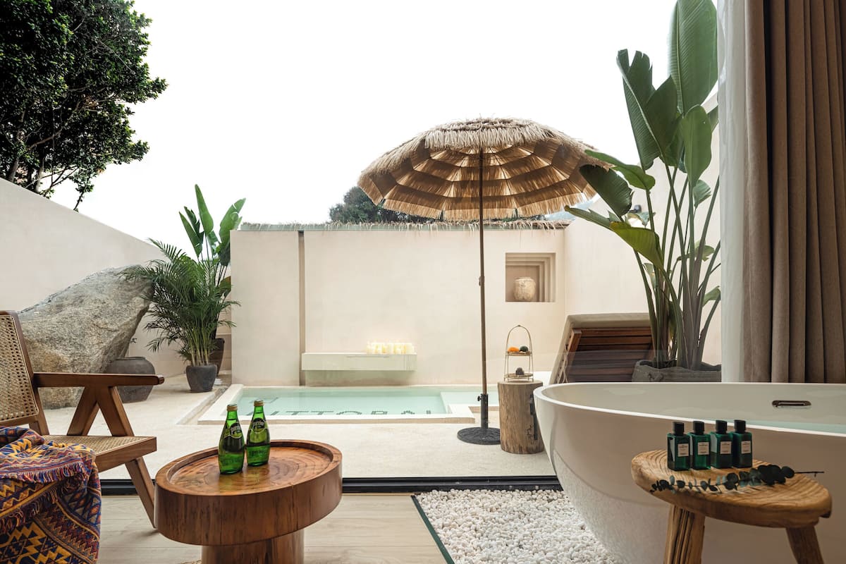 Een modern buitengebied met een zwembad, lounge stoelen, een houten tafel met flessen en een grote parasol.