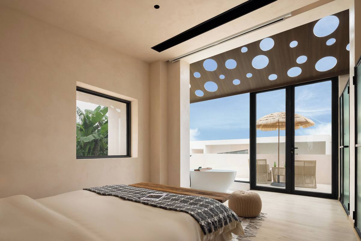 Een moderne slaapkamer met een groot bed, uitzicht op een balkon met een badkuip, en een houten plafond.