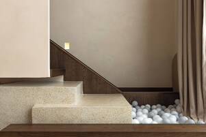 Una escalera con barandilla de madera y piso blanco moteado que baja a un nivel inferior.