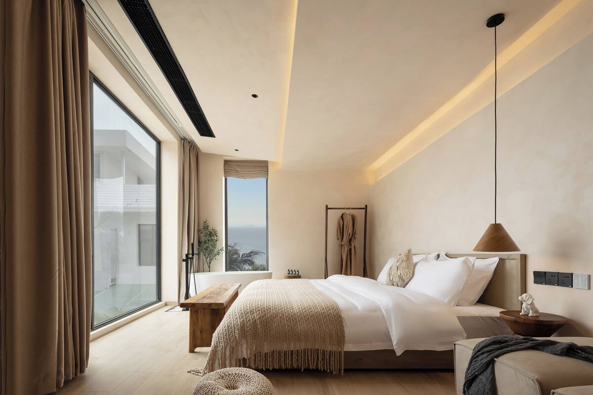 Een moderne slaapkamer met een groot bed, een houten nachtkastje, een hanglamp en uitzicht op de omgeving door een groot raam.