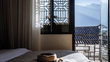 A hotel room with a bed, a hat on the bed, a window with a view of mountains, and a curtain.