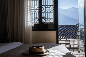 A hotel room with a bed, a hat on the bed, a window with a view of mountains, and a curtain.