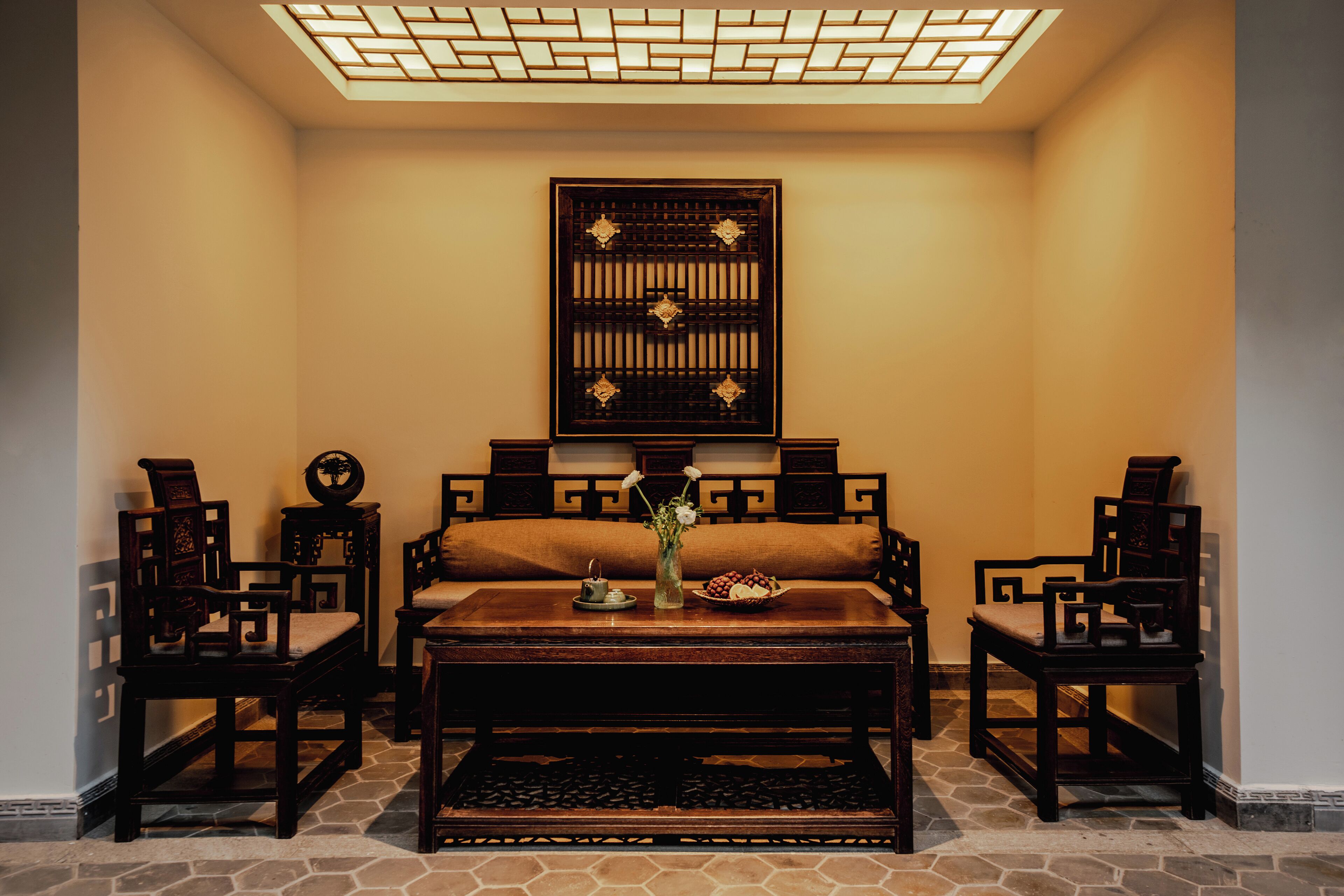 A traditional room with a sofa, two wooden chairs, a coffee table, and a decorative wall piece.