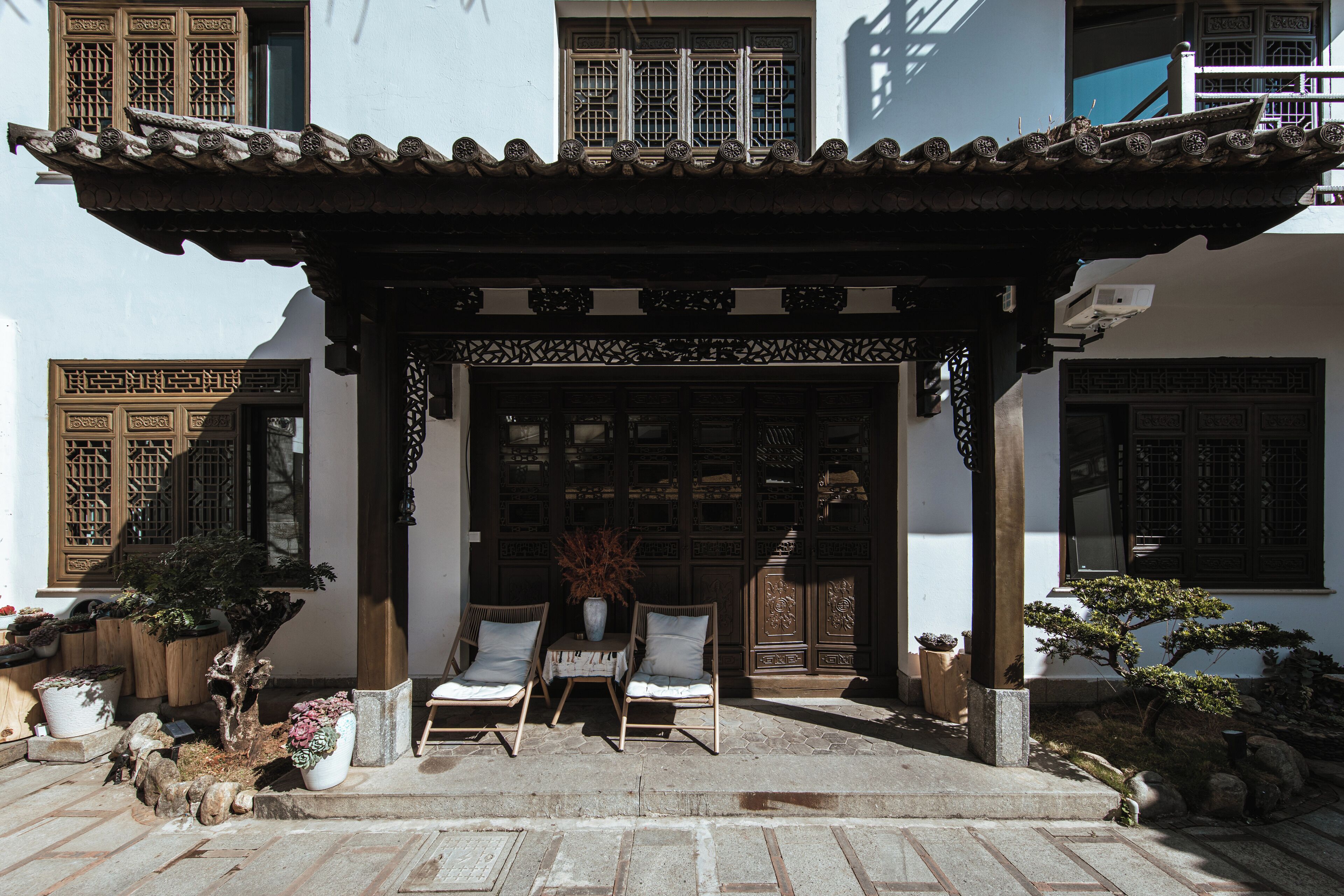 Um edifício tradicional chinês com telhado telhado, portas de madeira e uma entrada coberta com duas cadeiras e uma mesa.