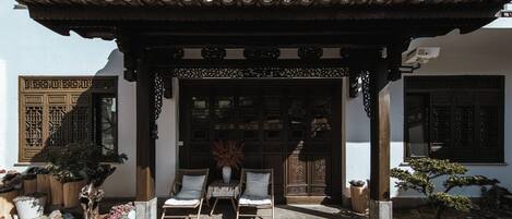 Um edifício tradicional chinês com telhado telhado, portas de madeira e uma entrada coberta com duas cadeiras e uma mesa.