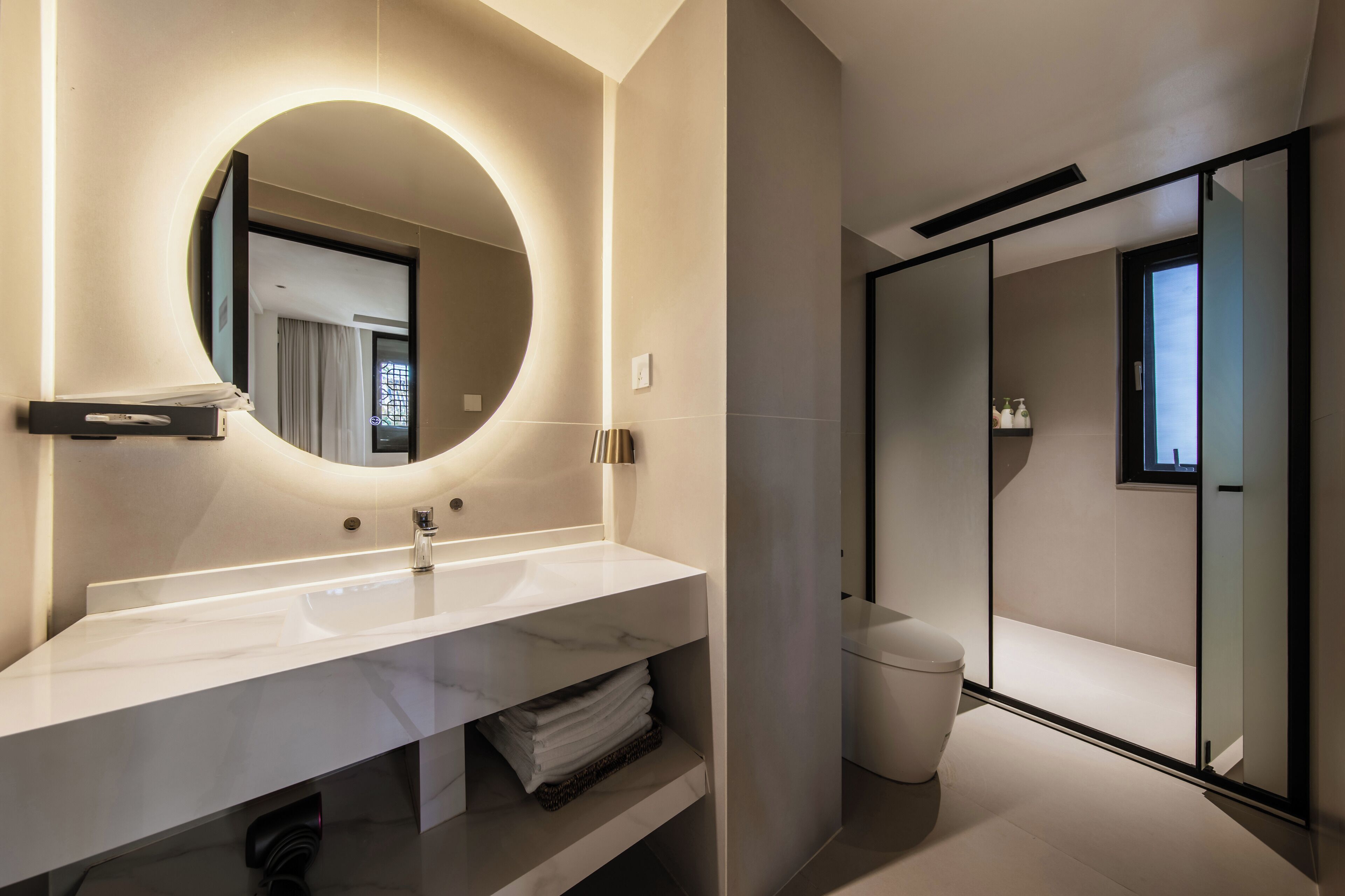 A modern bathroom with a large round mirror, a white sink, and a glass-enclosed shower area.