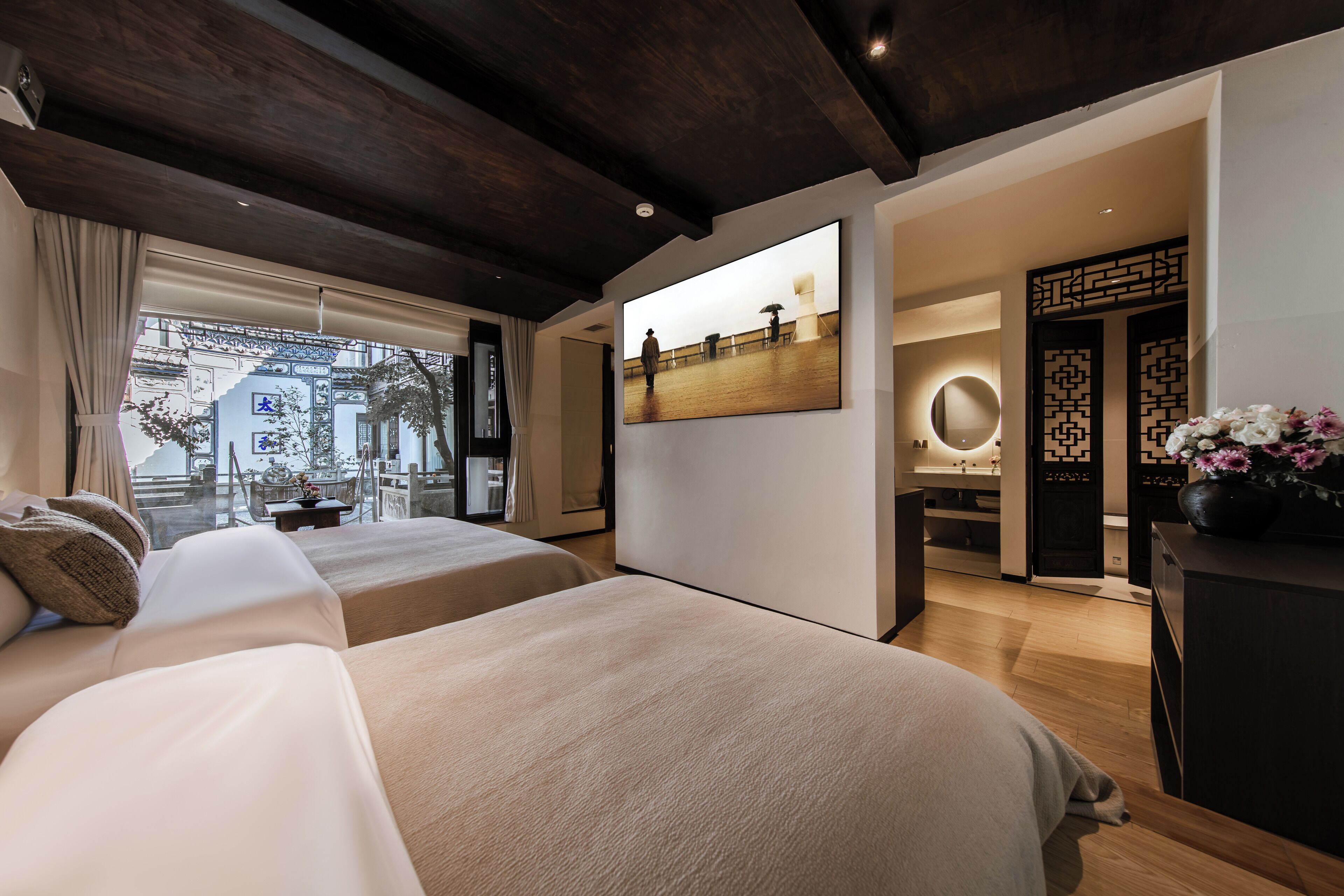 A modern hotel room with a large bed, a desk, and a view of a cityscape through the window.